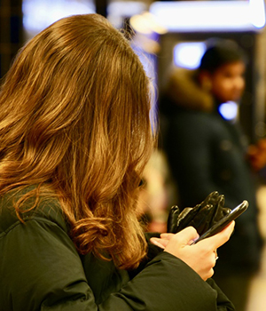 En kvinna står i en stadsmiljö och tittar på sin mobiltelefon. Håret döljer hennes ansikte.
