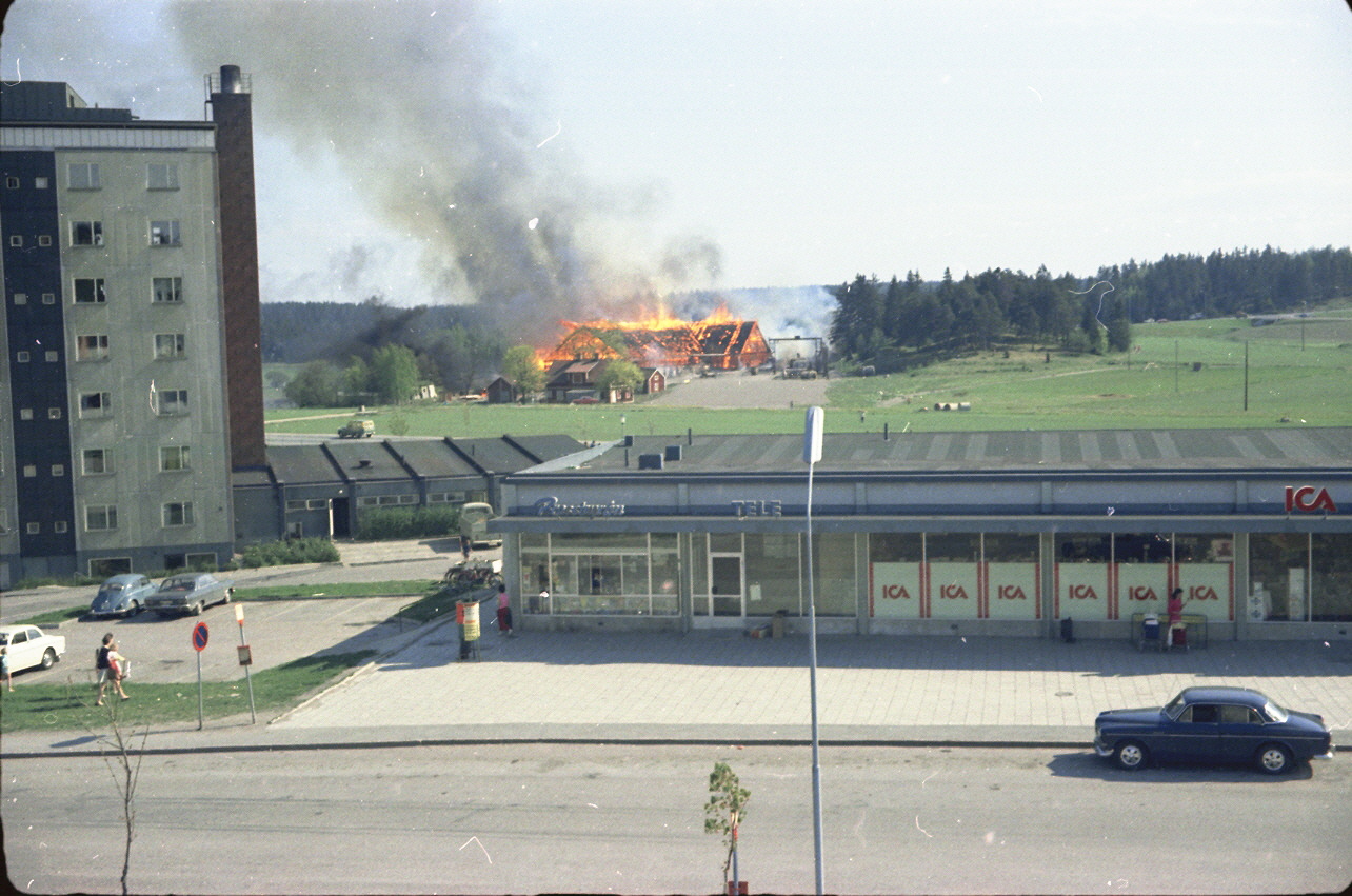 Bakom IKA brinner en lada på andra sidan gärdet.