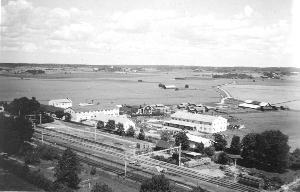 Ett svartvitt foto från hög höjd som visar tågspåren och några industribyggnader.