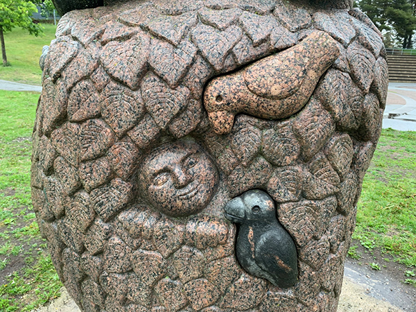 Skulptur i sten. I stenblocket syns former av ett ansikte, fåglar och blad.