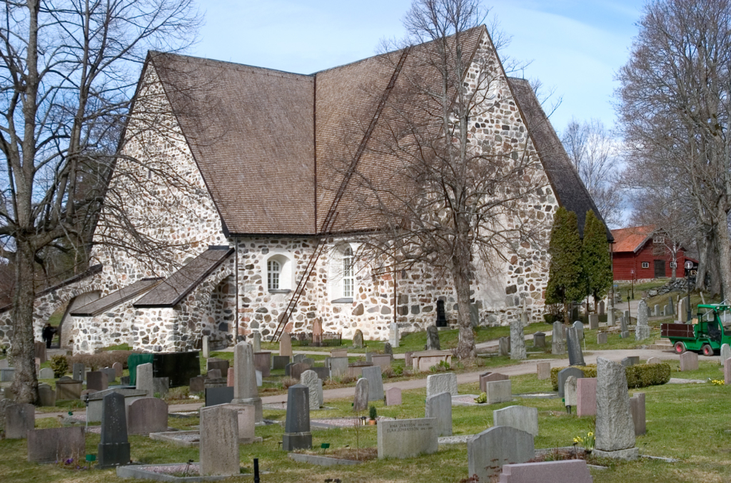 I bildens förgrund syns gravstenar och i bakgrunden Värmdö kyrka med sin stenfasad