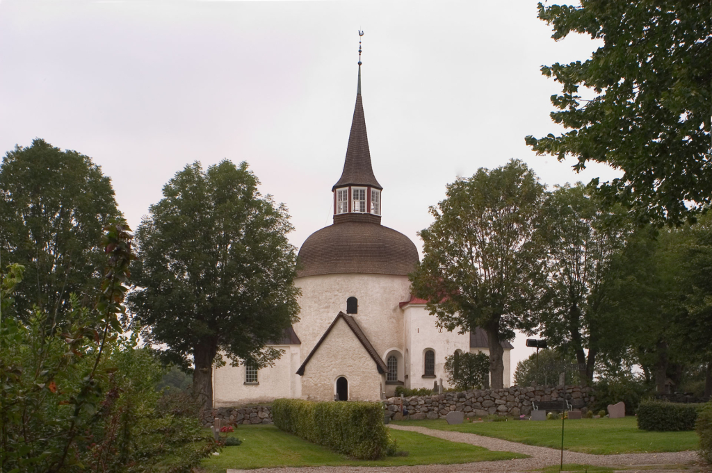 Munsö kyrkas fasad syns i mitten av bilden, bakom några trädkronor.
