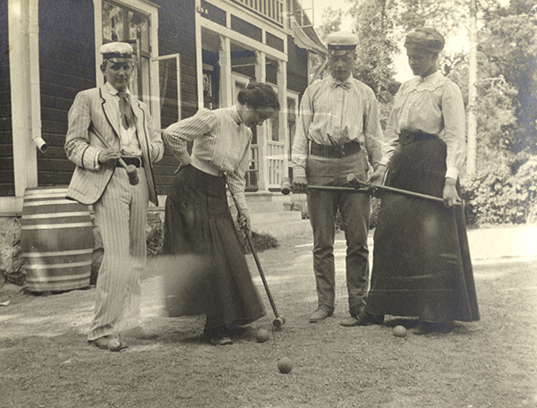 Historisk bild, fyra ungdomar spelar krocket. Kvinnorna har långa kjolar och männen studentmössor.