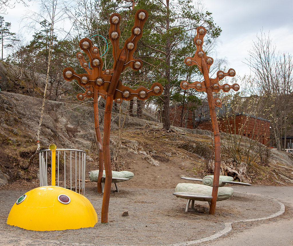 Lekskulptur som består av olika delar i skolmiljö. Skulpturerna i olika former och färger finns vid en bergsknalle. En knallgul rundad form som liknar en val med två lampor är längst fram. Bakom denna är två höga skulpturer med bruna former liknande tång som delar sig högst upp och spretar åt olika håll, och tre låga gröna sittskulpturer som har ljusgröna vingar och liknar små flygplan.