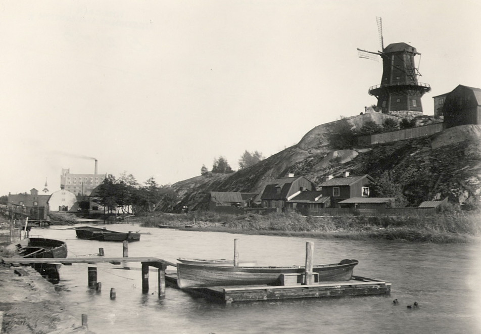 Svartvitt foto av en kvarn på en bergknalle över vattnet.