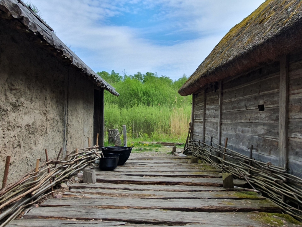 Färgfoto av två hus med ett brädgolv mellan.