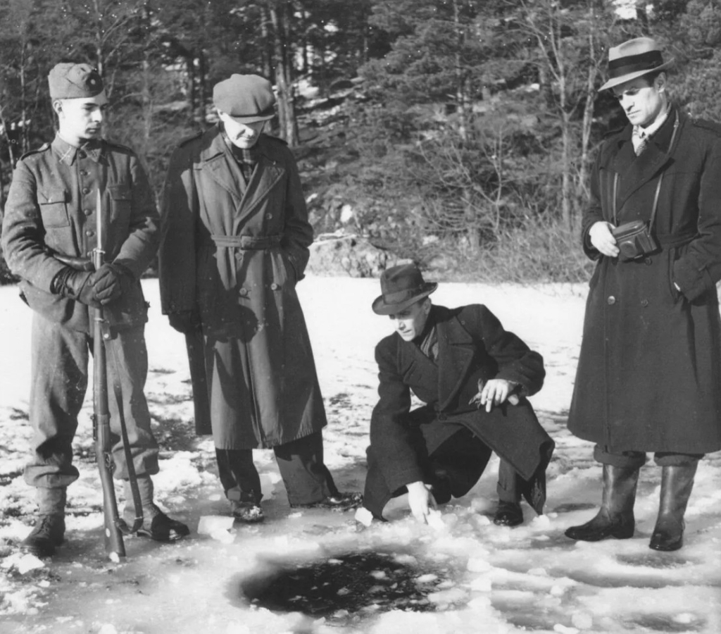 Fyra män vid en isvak. En är iförd militära kläder och har ett gevär. De andra civila.