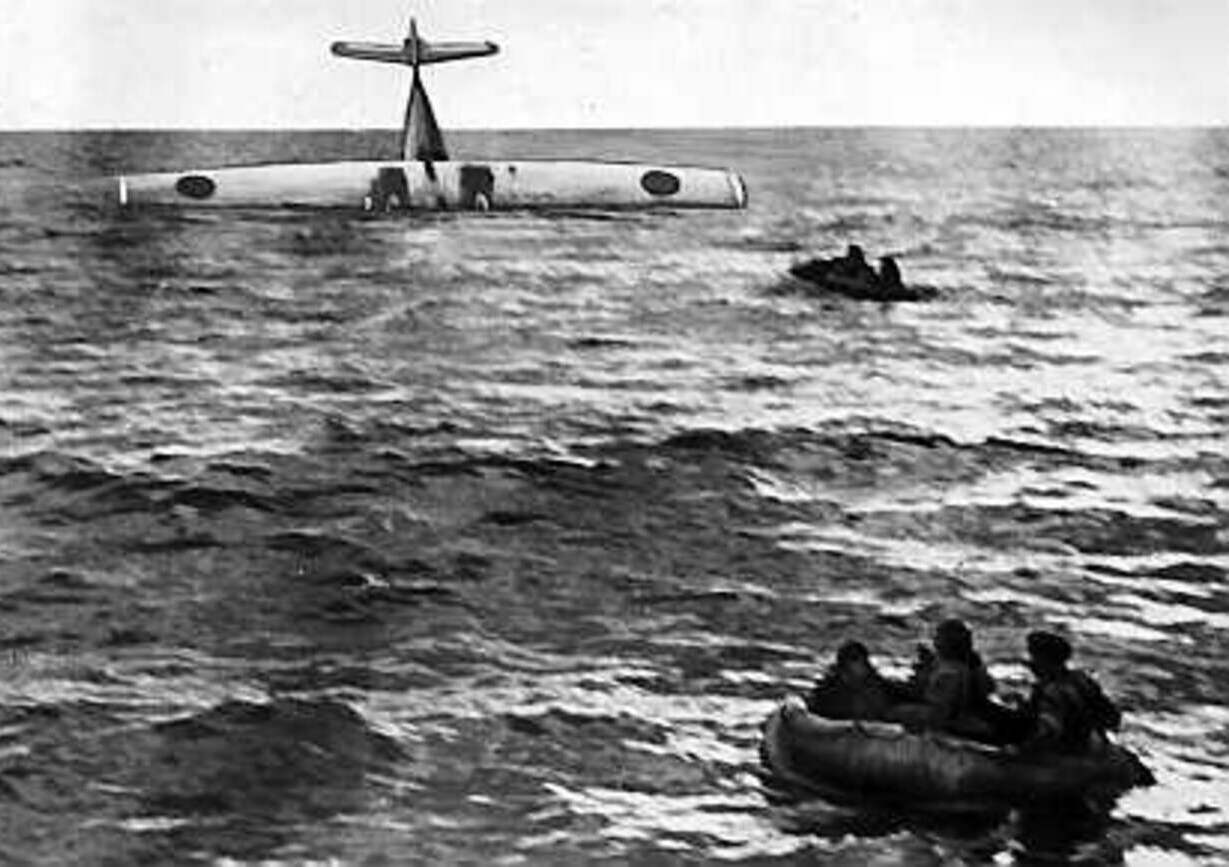 Flygplanet har nosen ner i havet. Förutom planet syns bara hav, horisont och två små livflottar.