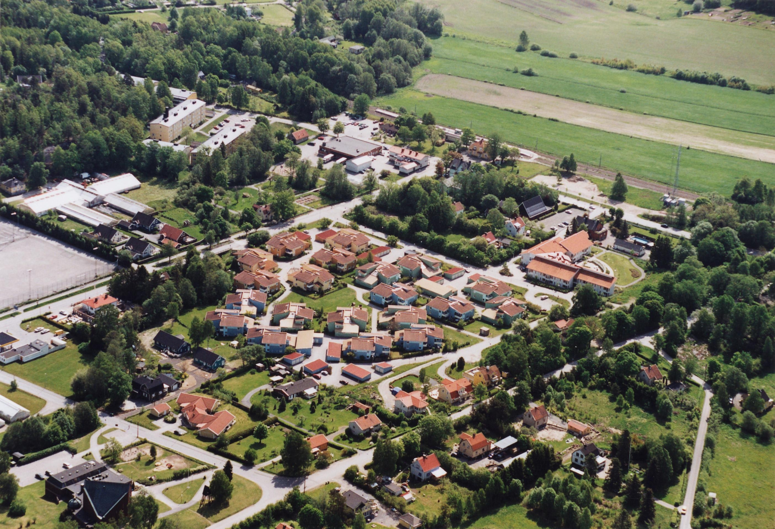 Flygfoto i färg. Bebyggelsen i tungelsta slutar tvärt och på bortre sidan av järnvägen breder en åker ut sig.