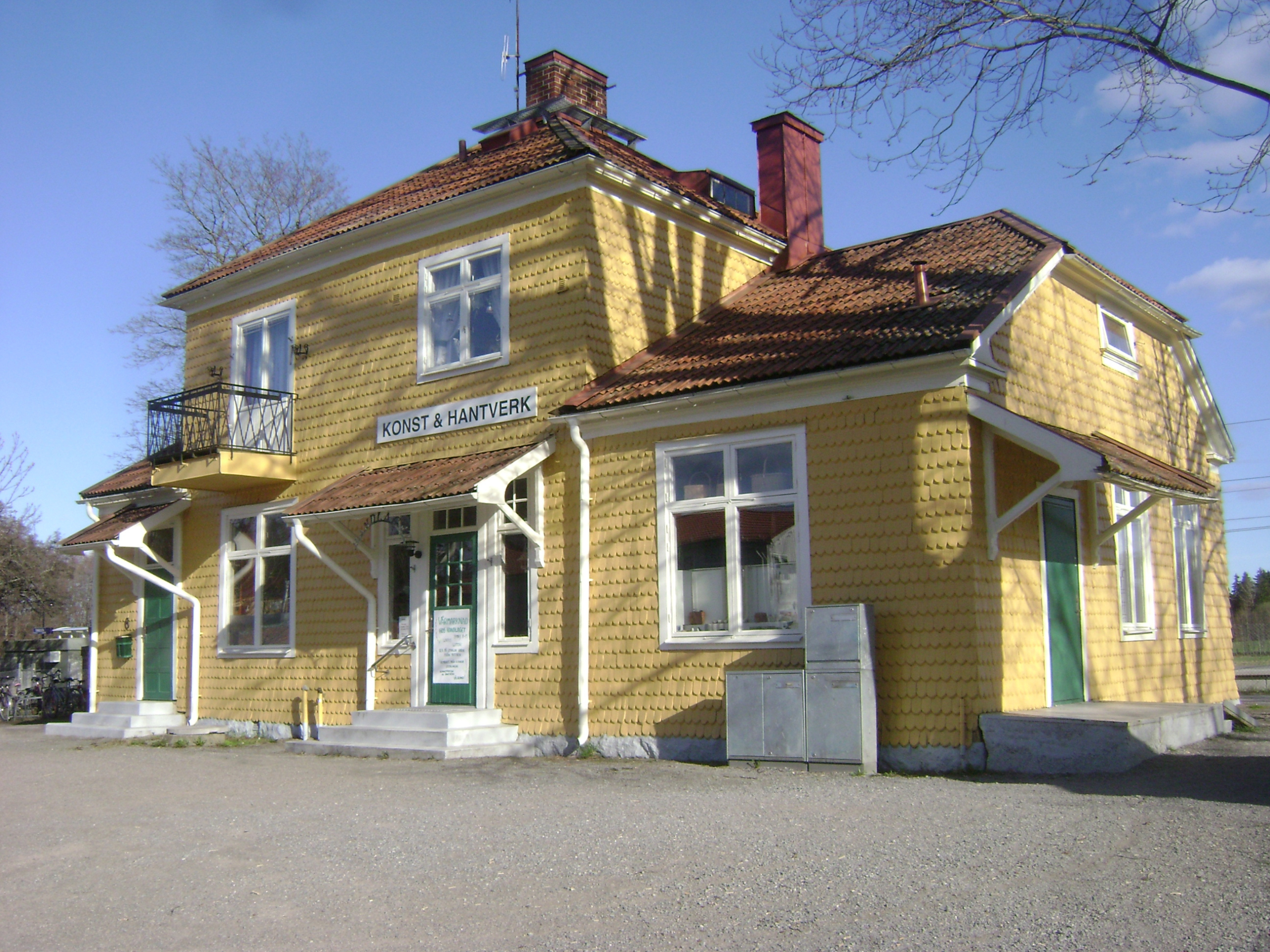 Ett färgfoto av det gula stationshuset i trä med toppigt tak, balkong, två våningar.