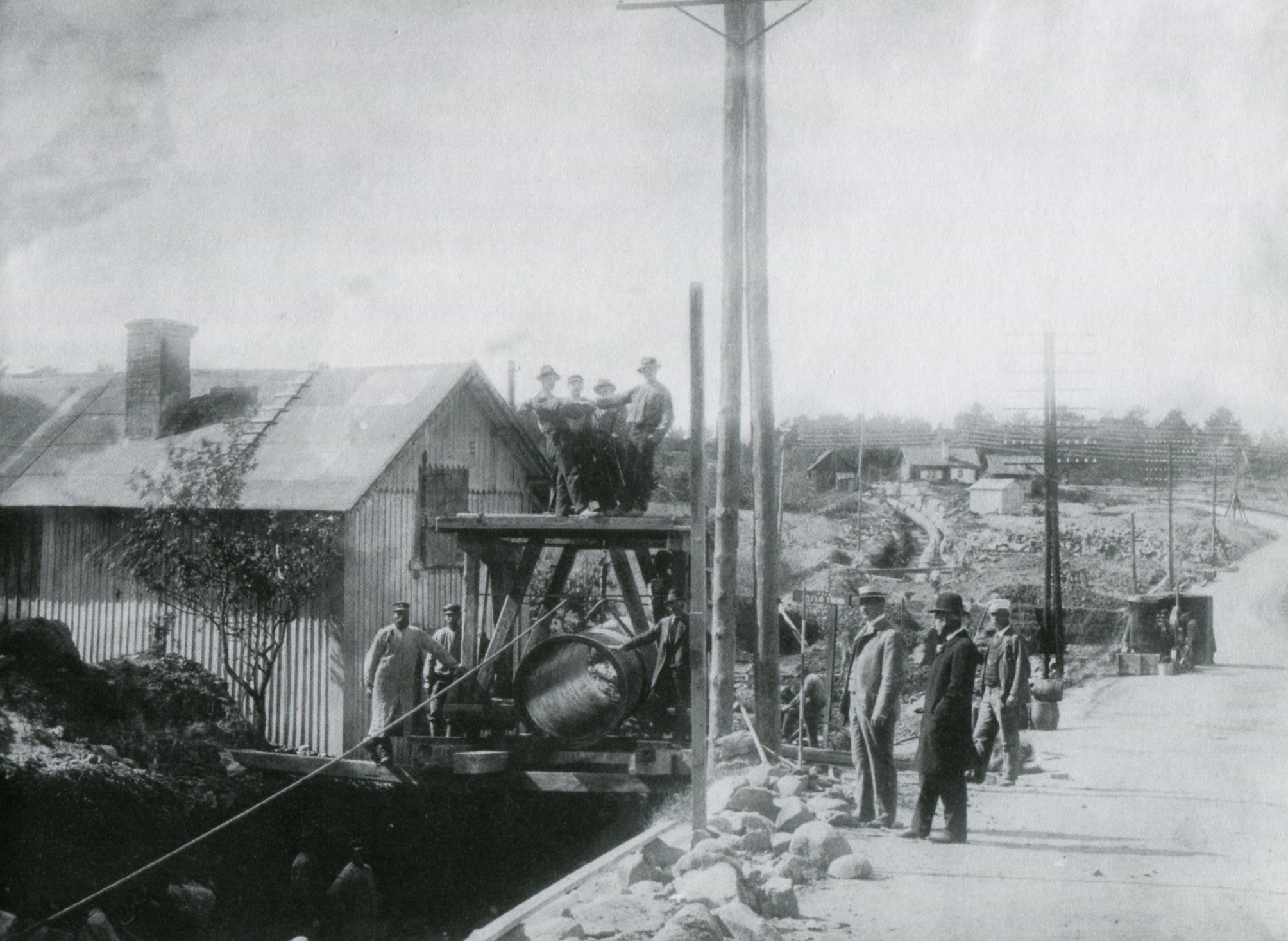 En grupp män runt vattenledningen. Längre bort i bilden ligger den i en grävd ränna.