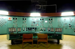 Kontrollrum med gröna paneler, lysramp i trä och två trästolar vid kontrollbordet.