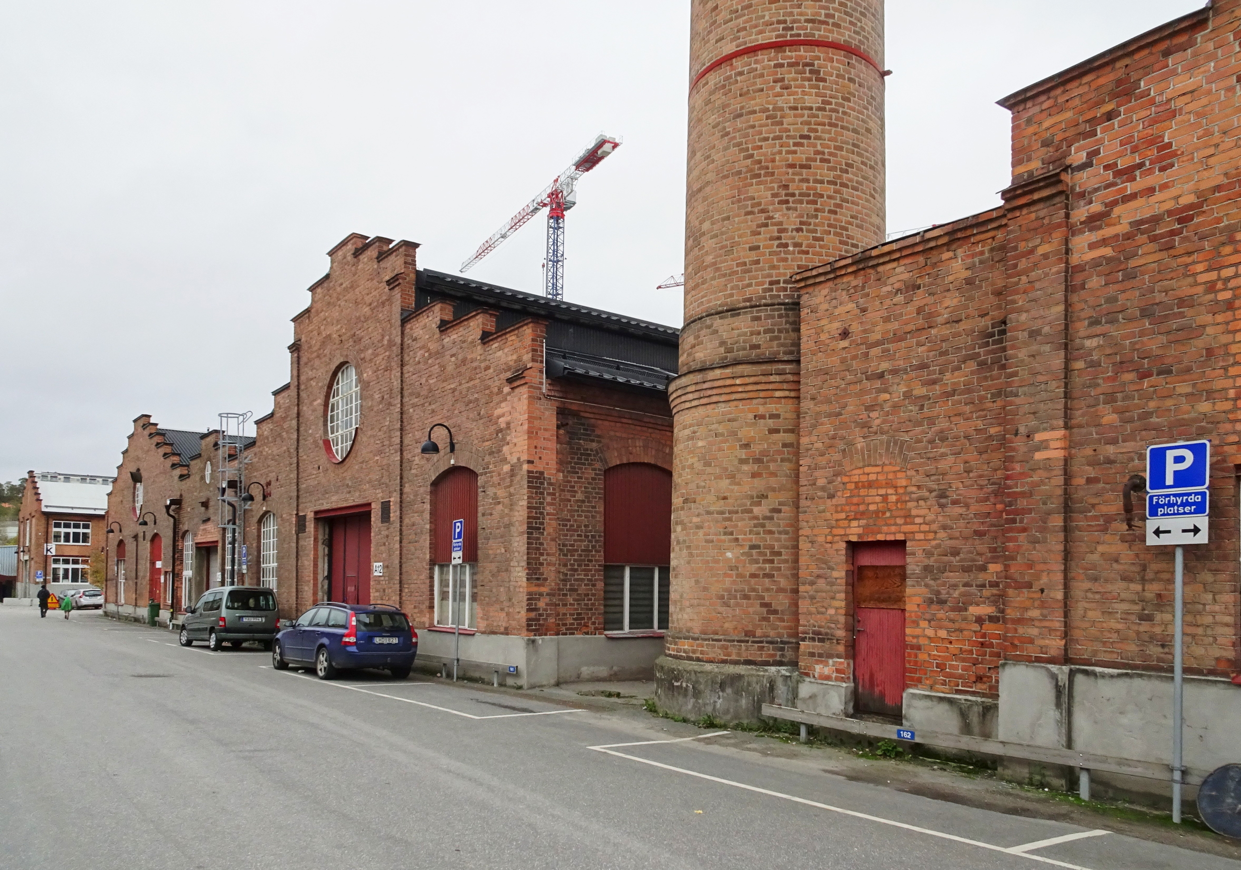 Två stora tegelbyggnader. En med en högskorsten. Ett par bilar står framför byggnaderna