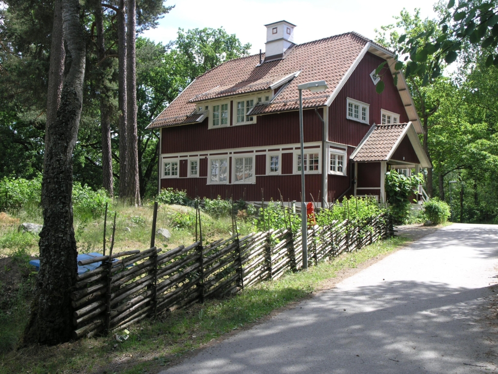 En röd villa med vita knutar. I förgrunden står en gärdsgård.