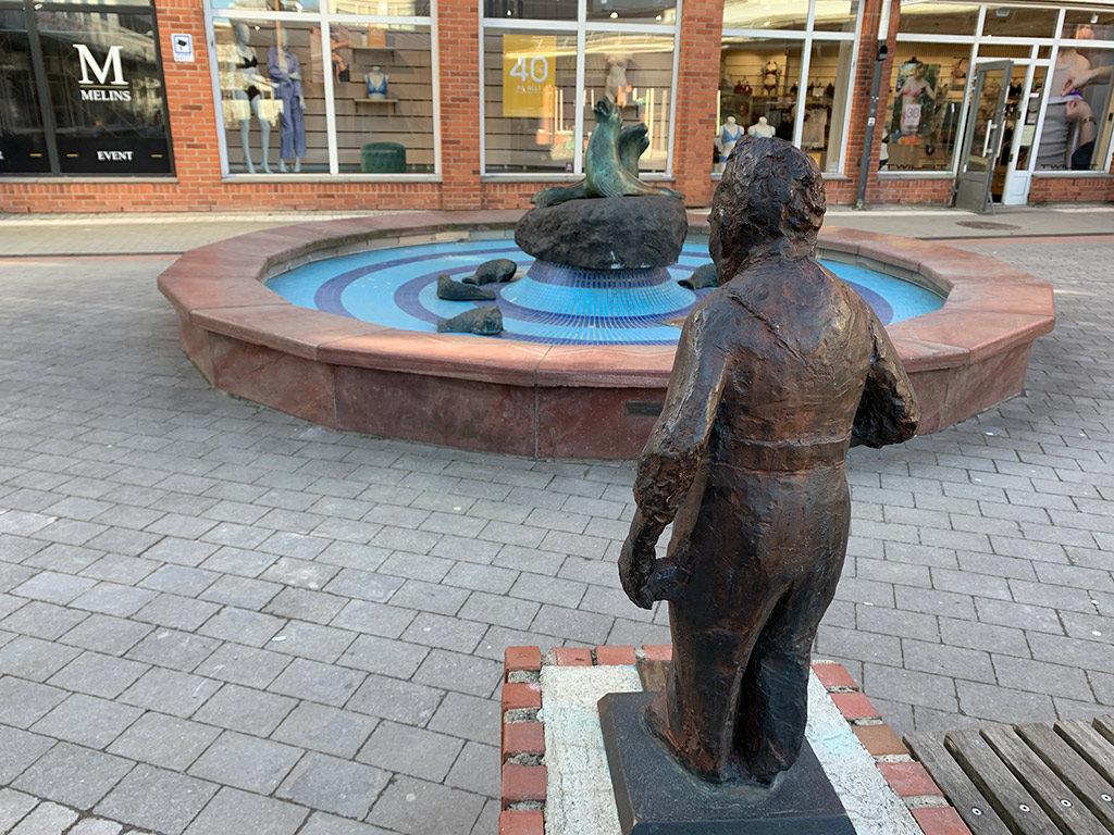 Skulptur av en man som ser på en fontän på ett torg,