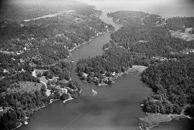 Flygbild. Smalt sund med skog på båda sidor.