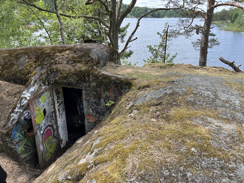 En dörr står öppen till den mossbevuxna betongbunkern vid vattnet. 