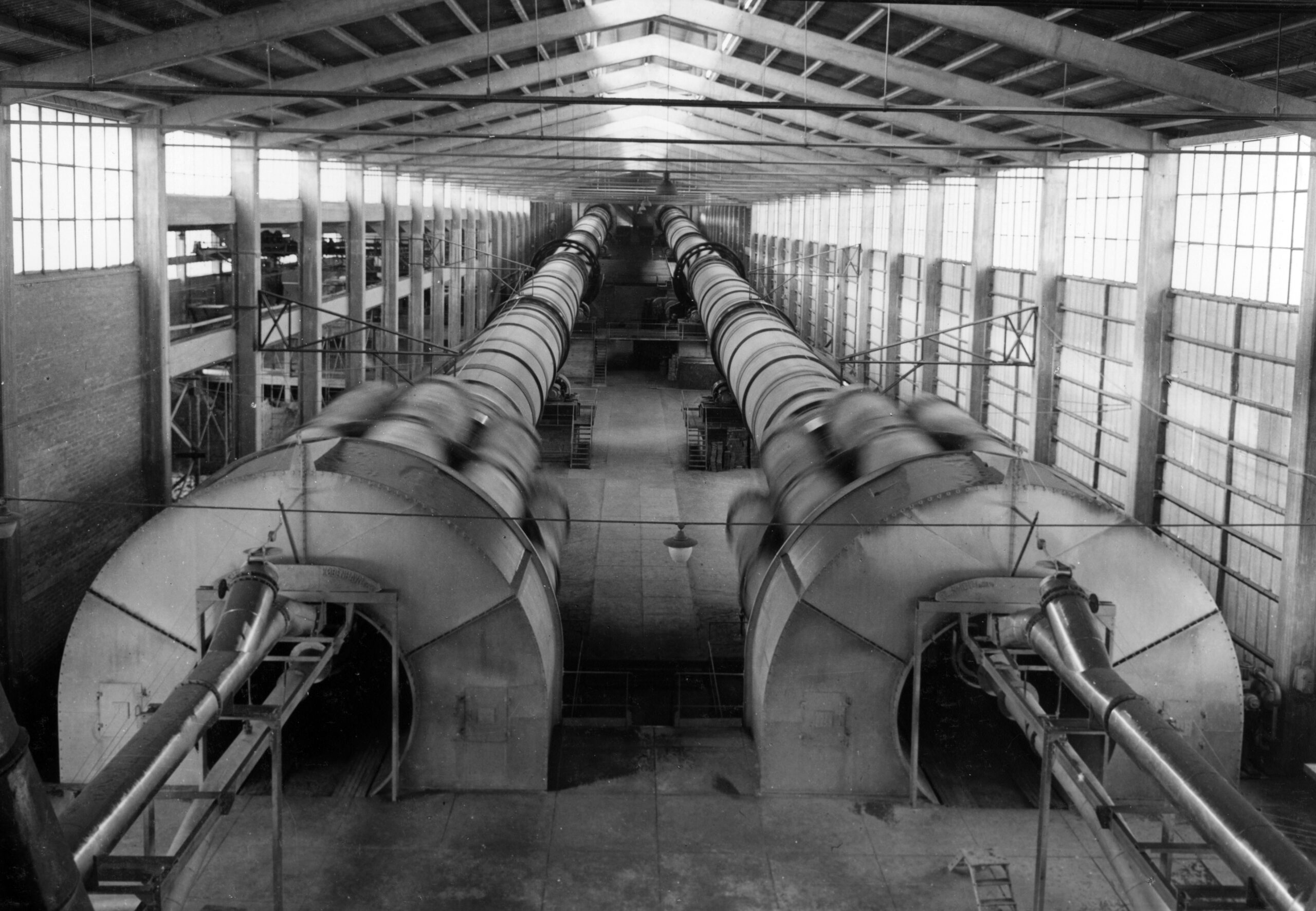 Två långa cylindrar upptar utrymmet i en långsmal industribyggnad med stora fönster under taket.