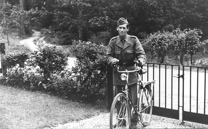 En man i uniform står med sin cykel vid en grind.