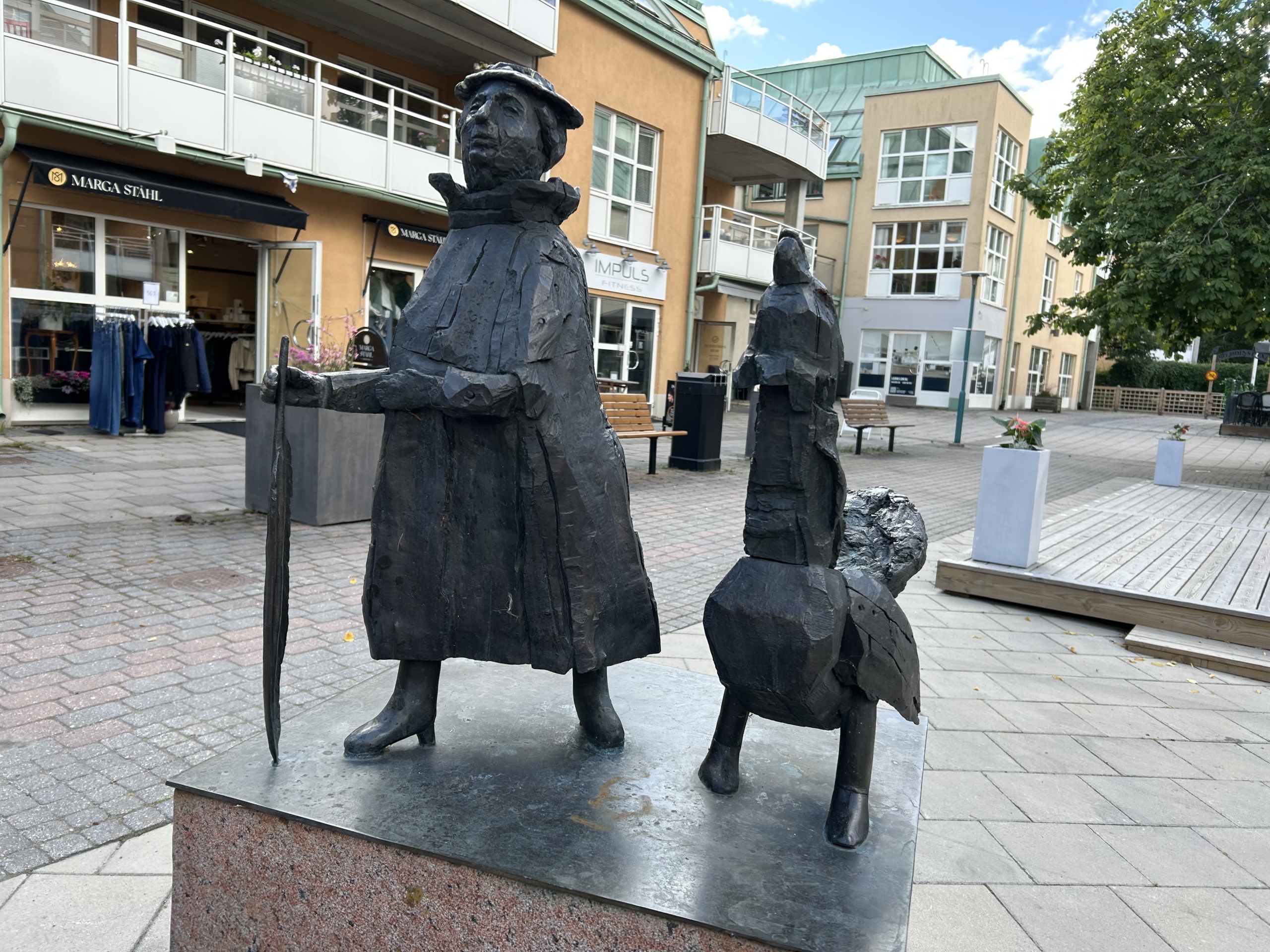 En skulptur av en dam klädd i kappa och hatt med en fjäder till käpp, i sällskap med en tjäder.