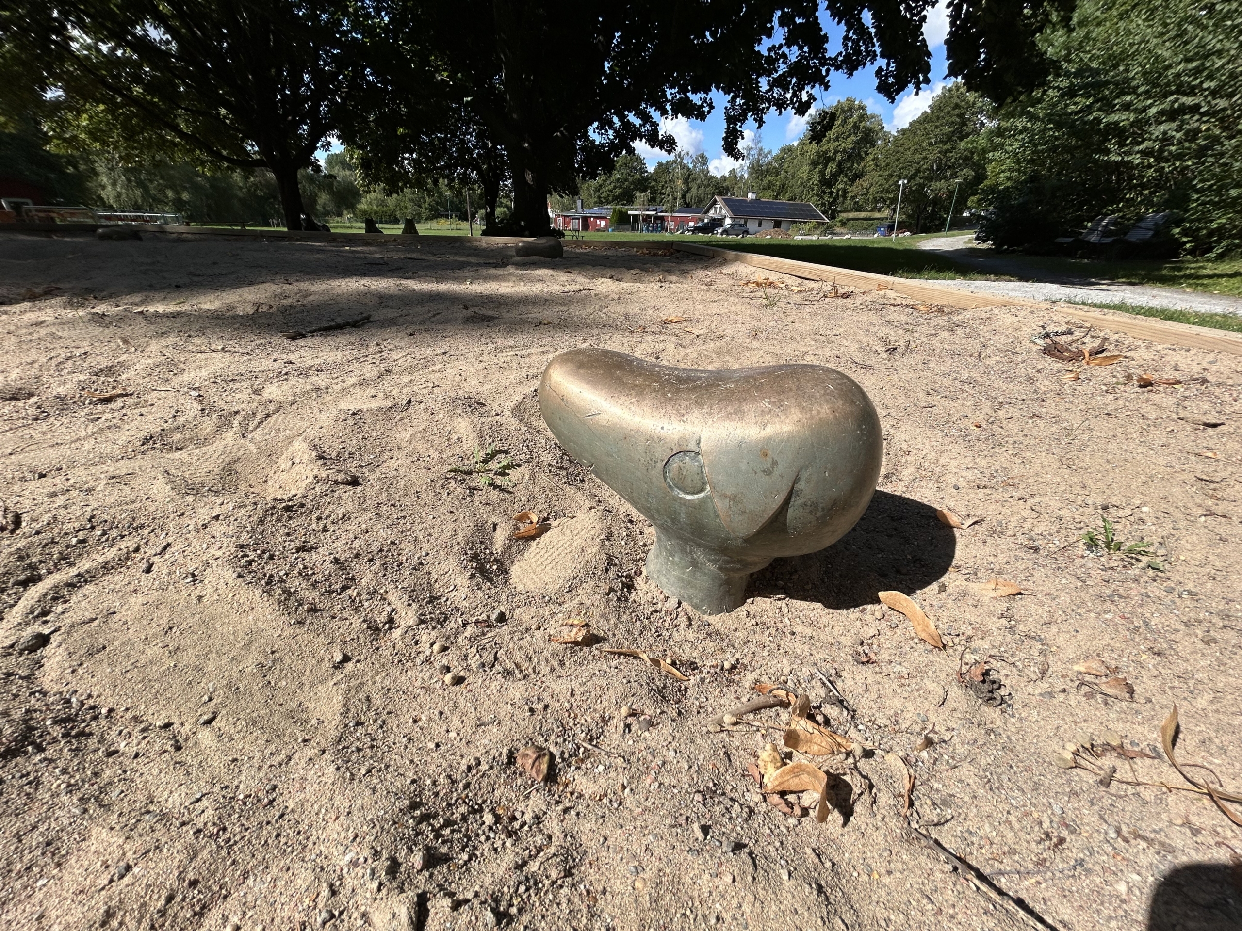 En gyllene skulptur av ett djurliknande avlång huvud med stora ögon som sticker upp ur en sandlåda.