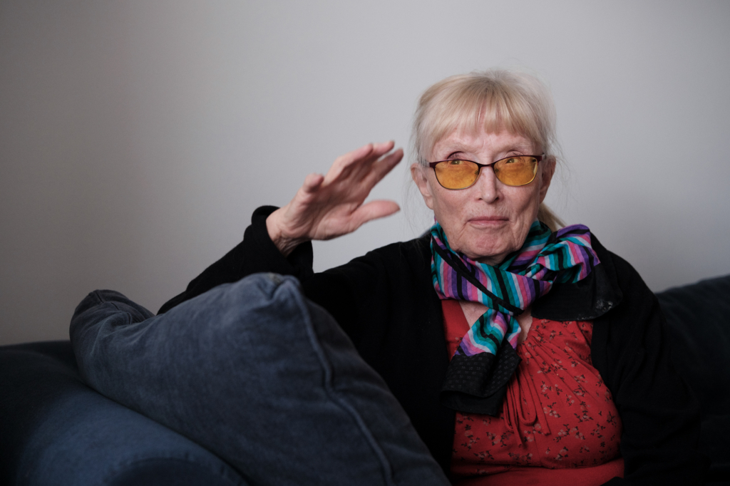 En kvinna i en soffa, hon höjer handen och ser ut att berätta någon.