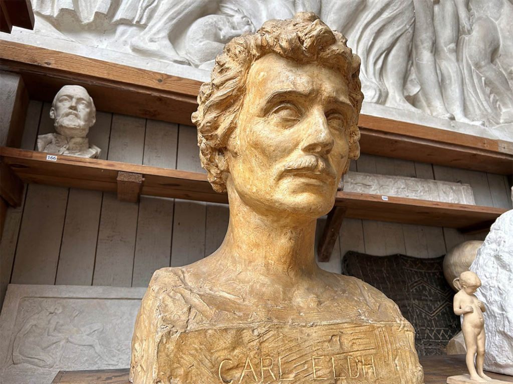 Skulptur av en man med yvigt hår och mustasch. Terrakottafärgad