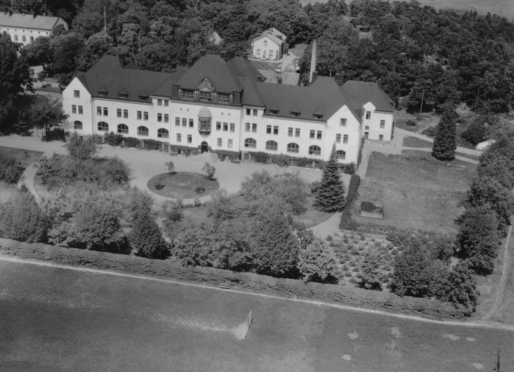 Flygfoto i svartvitt. Slottslik skolbyggnad.
