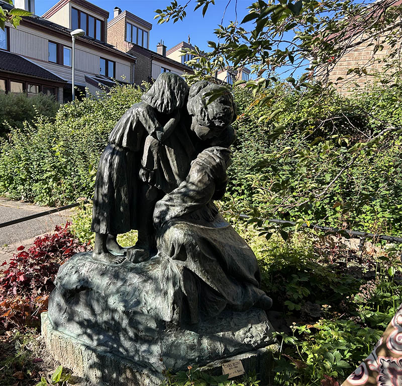 Skulpturgrupp med kvinna och två barn i en grönskande park.