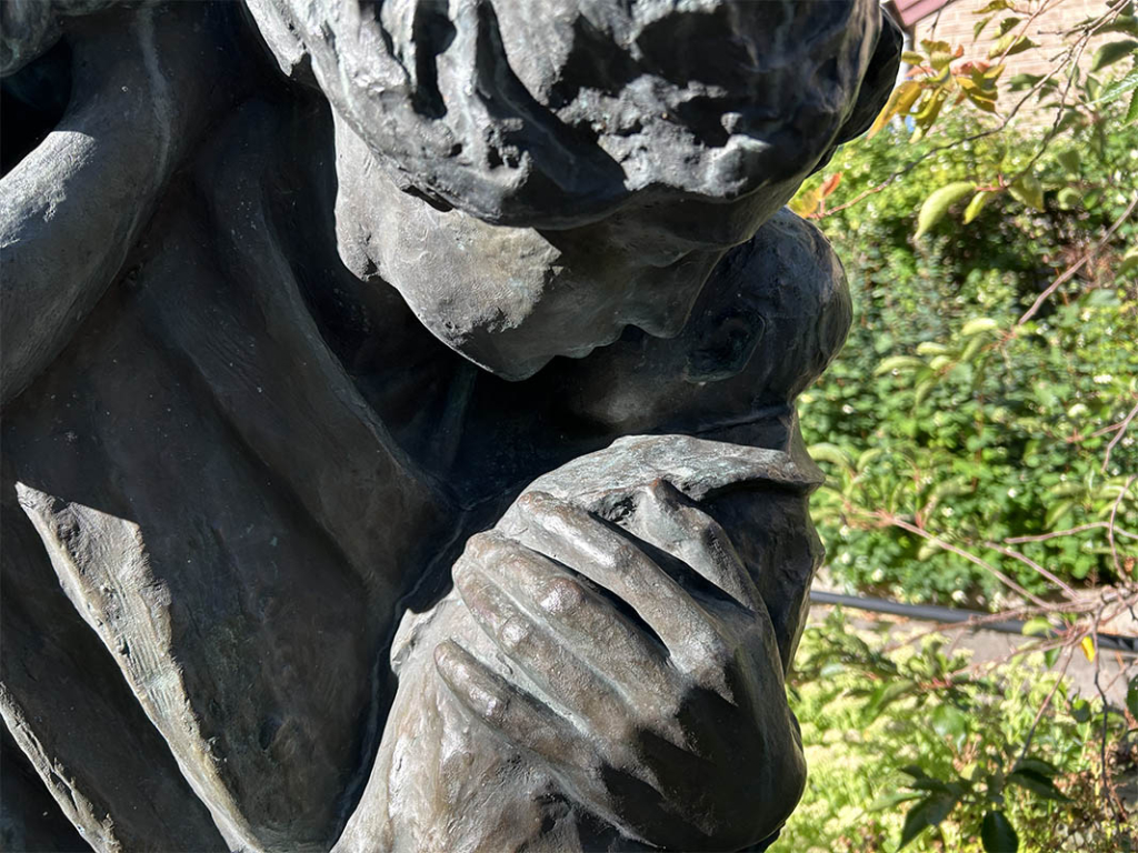 Skulptur med kvinna och barn i en grönskande omgivning.