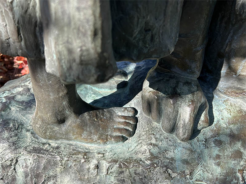 Skulptur i brons med barnfot och en och knuten näve. Detalj av en skulptur.