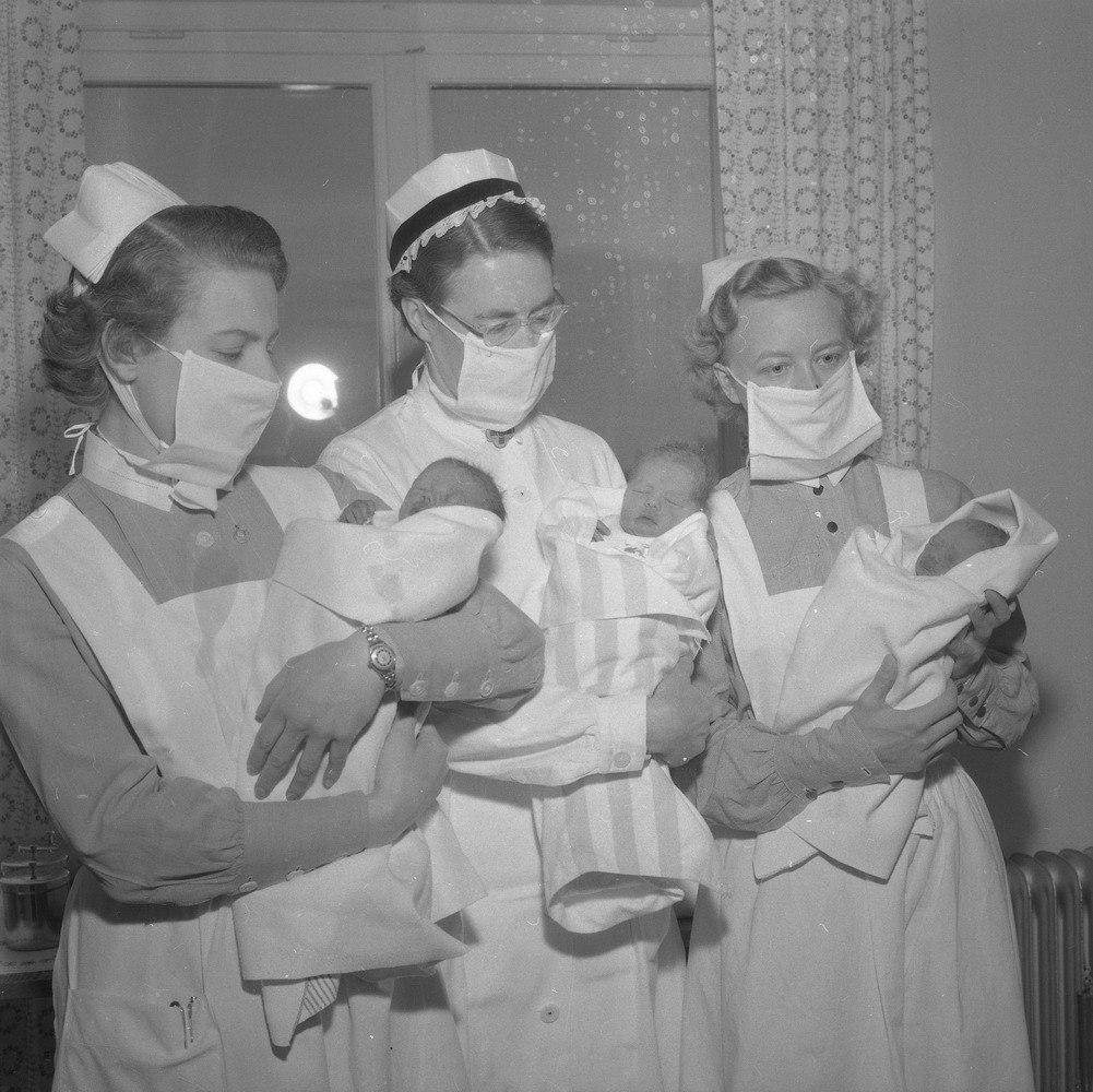 Tre sköterskor på rad med nyfödda bebisar i famnen.