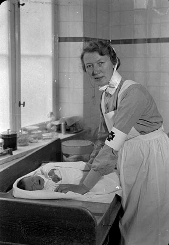 En barnmorska står böjd över en bebis på en bänk.