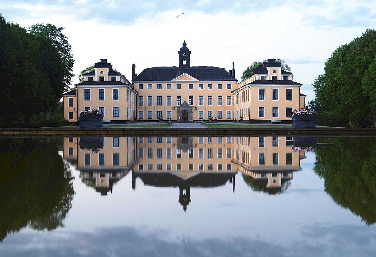 Slottsbyggnad som speglas i vatten.