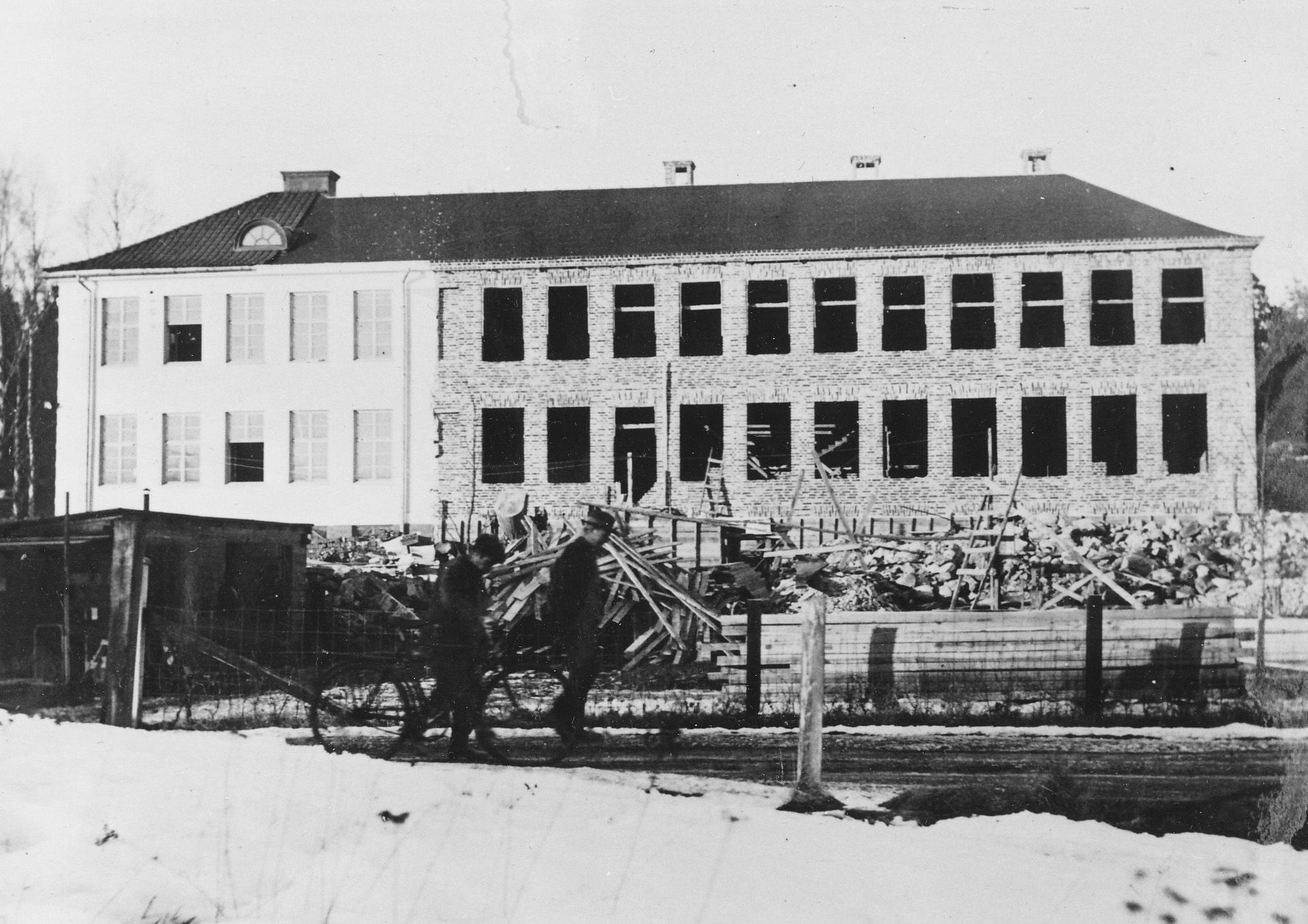 En svartvit bild av skolan med tillbyggnaden med tomma fönstergluggar.