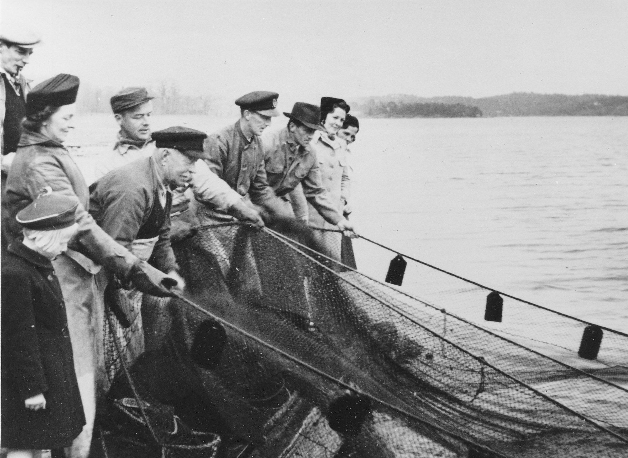 Nio personer på rad drar i ett nät som ligger i vattnet.