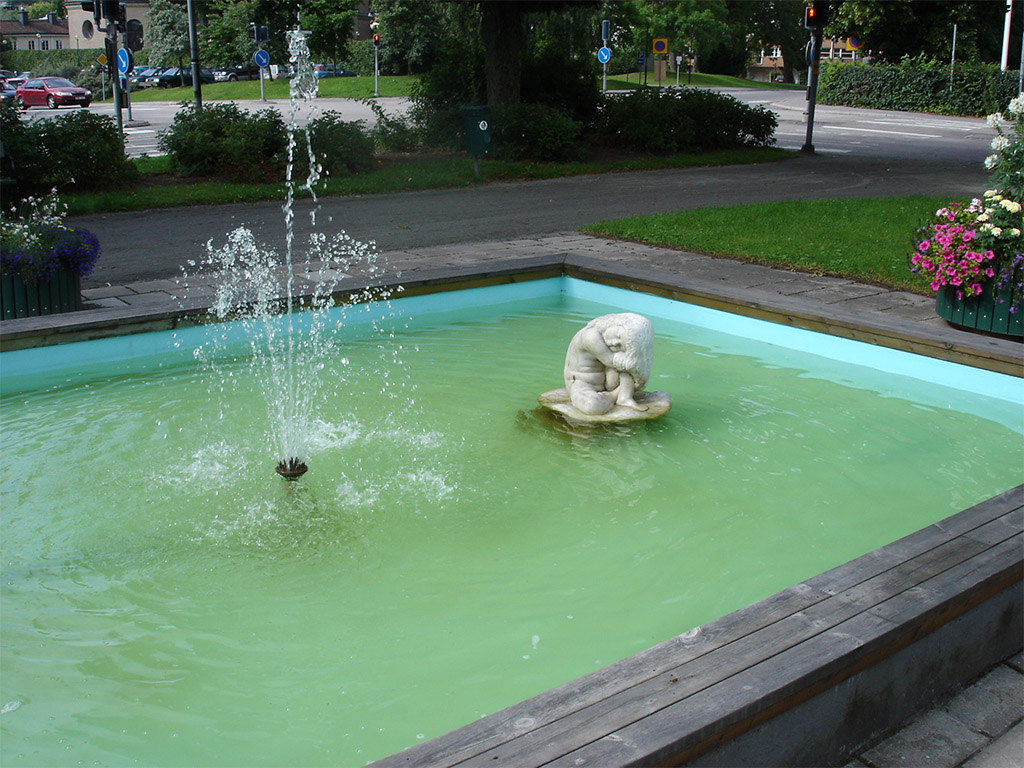 Vit skulptur av en flicka en fyrkantig damm.