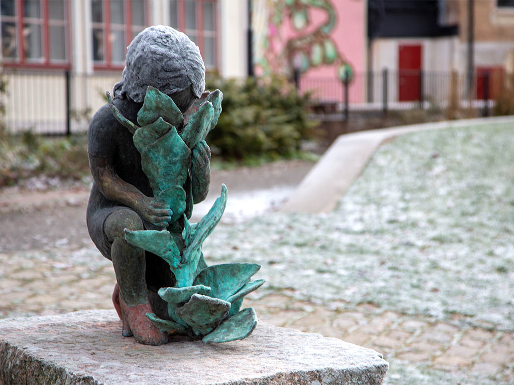 Skulptur av en flicka som gömmer ansiktet i en blomma.
