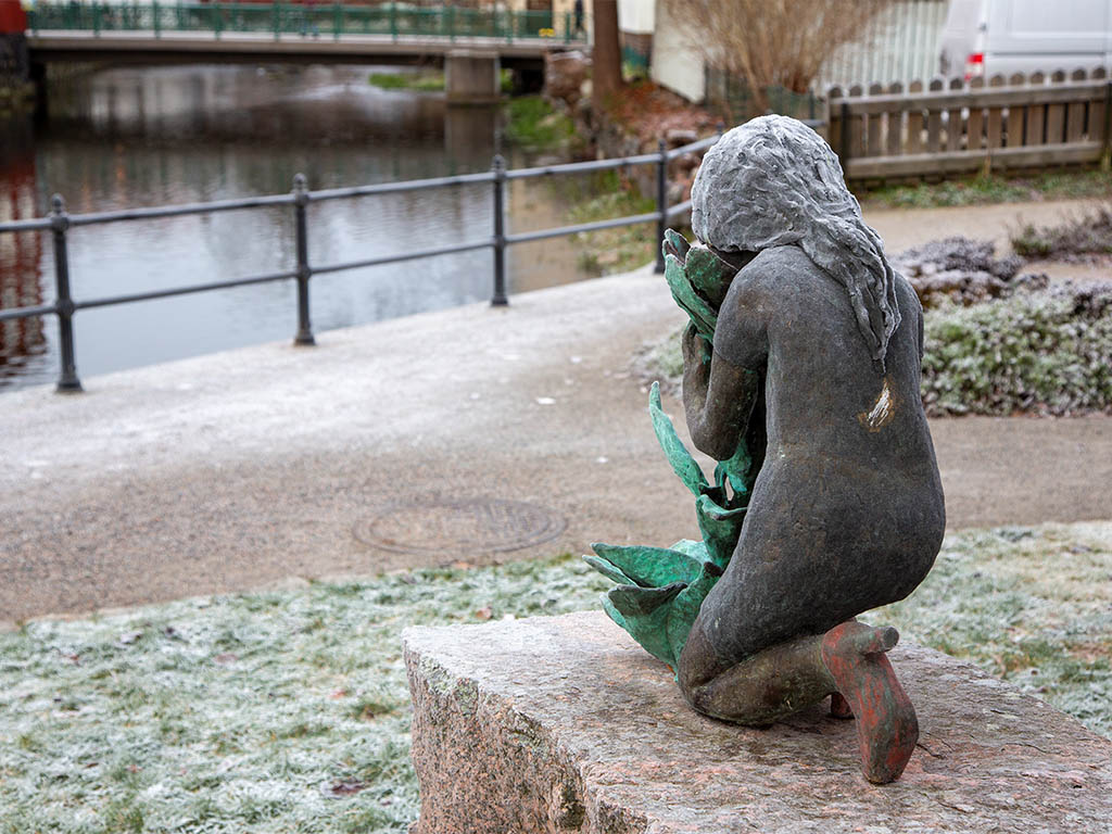 Skulptur av en flicka bakifrån framför en å.