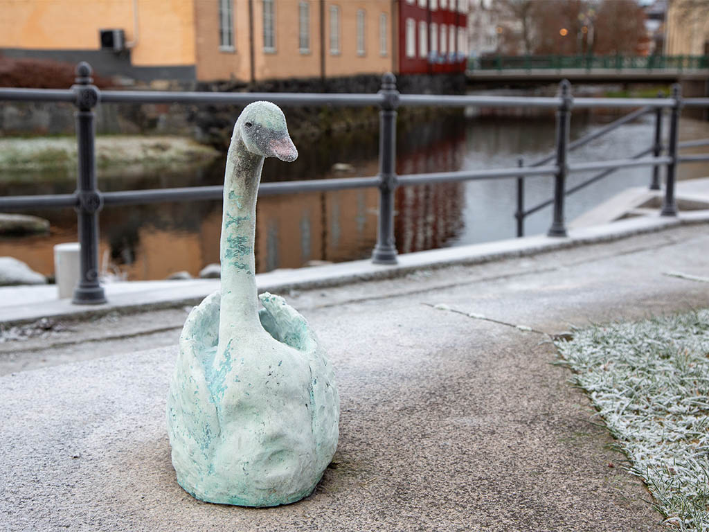 Skulptur av en vit svan vid en å.