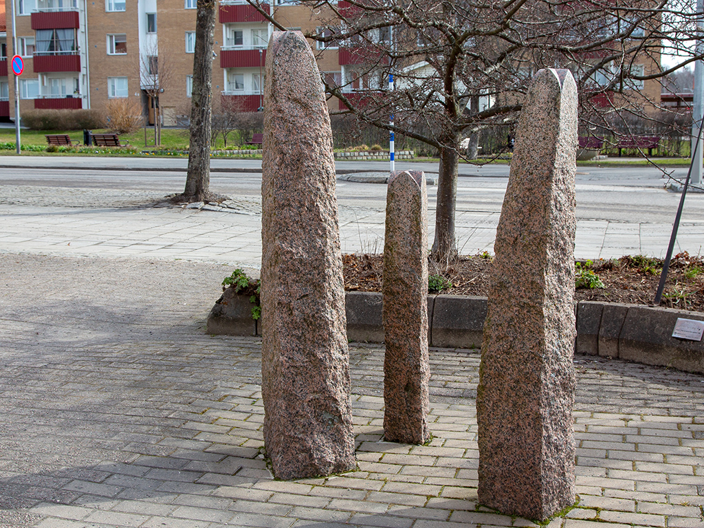 Tre höga smala stenar som står på en markbeläggning av sten vid en gata.