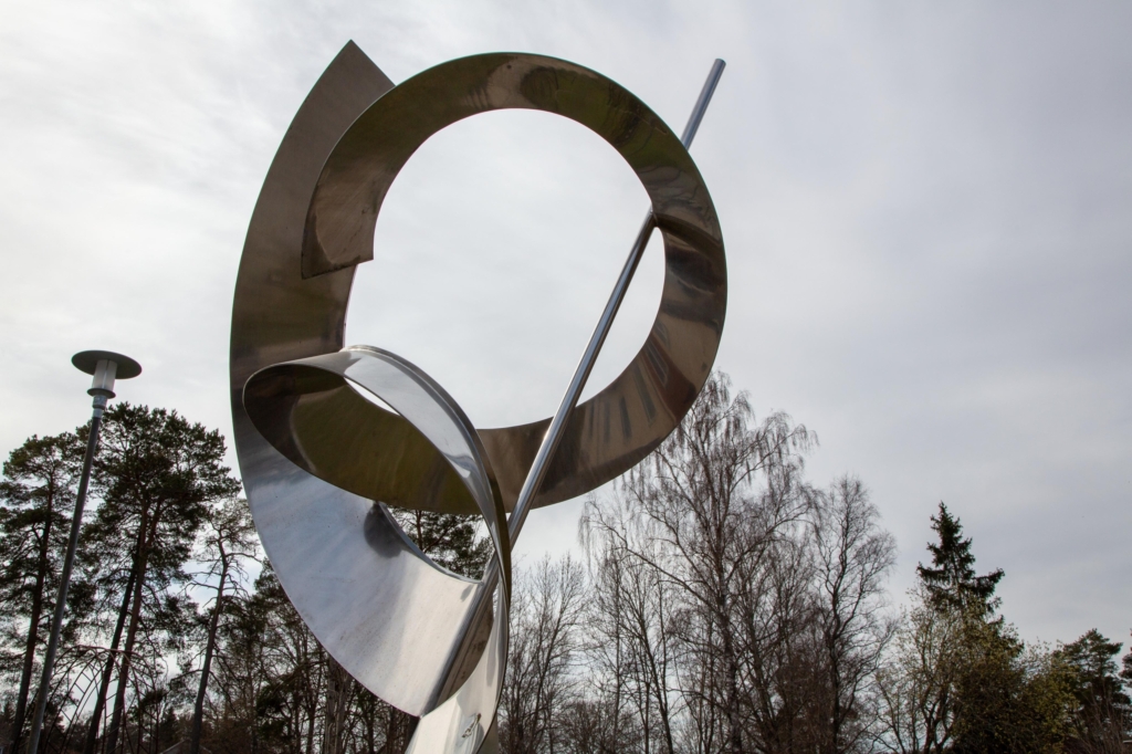 Abstrakt skulptur i stål mot en grå himmel.