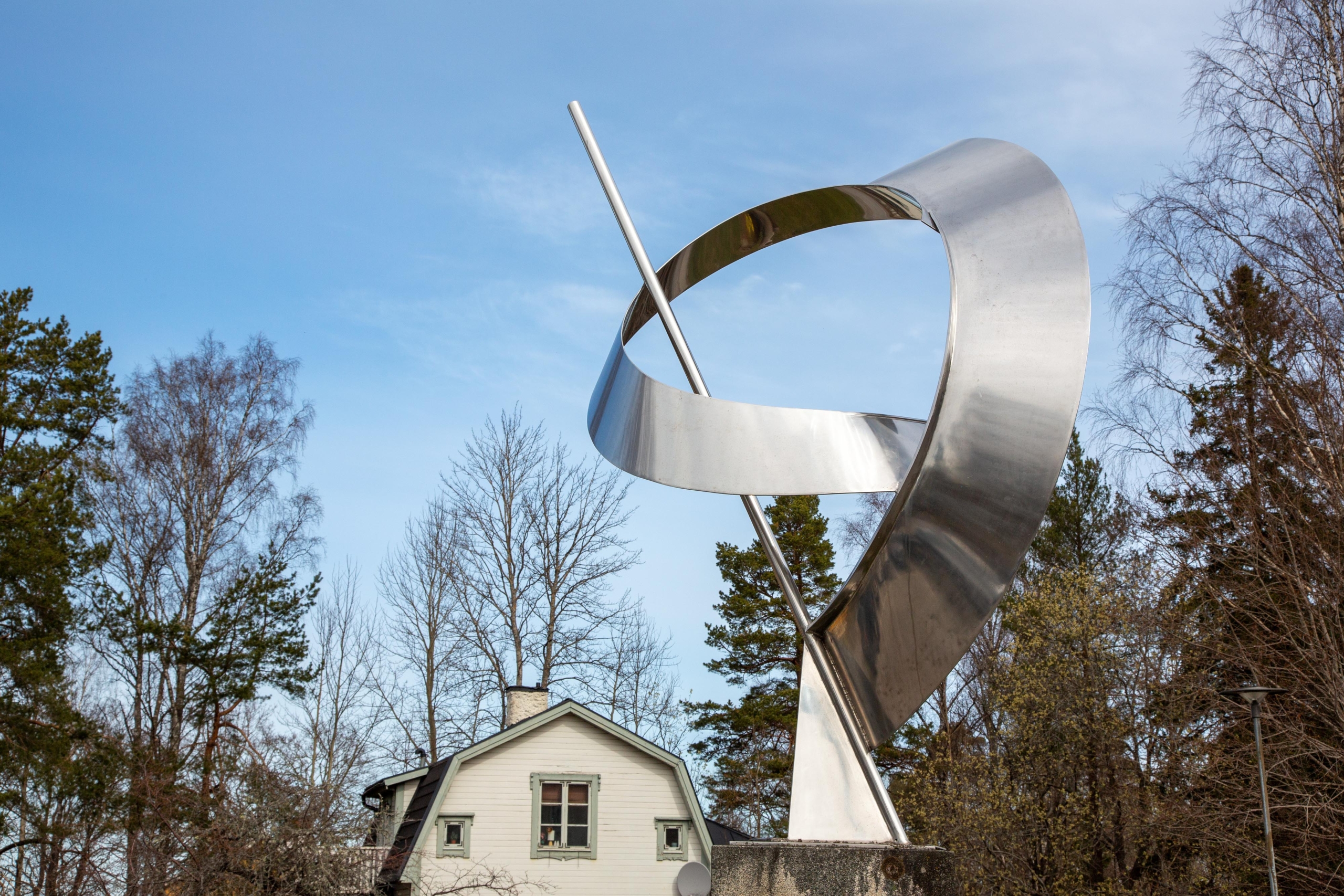 Blänkande abstrakt skulptur i stål mot en ljusblå himmel.