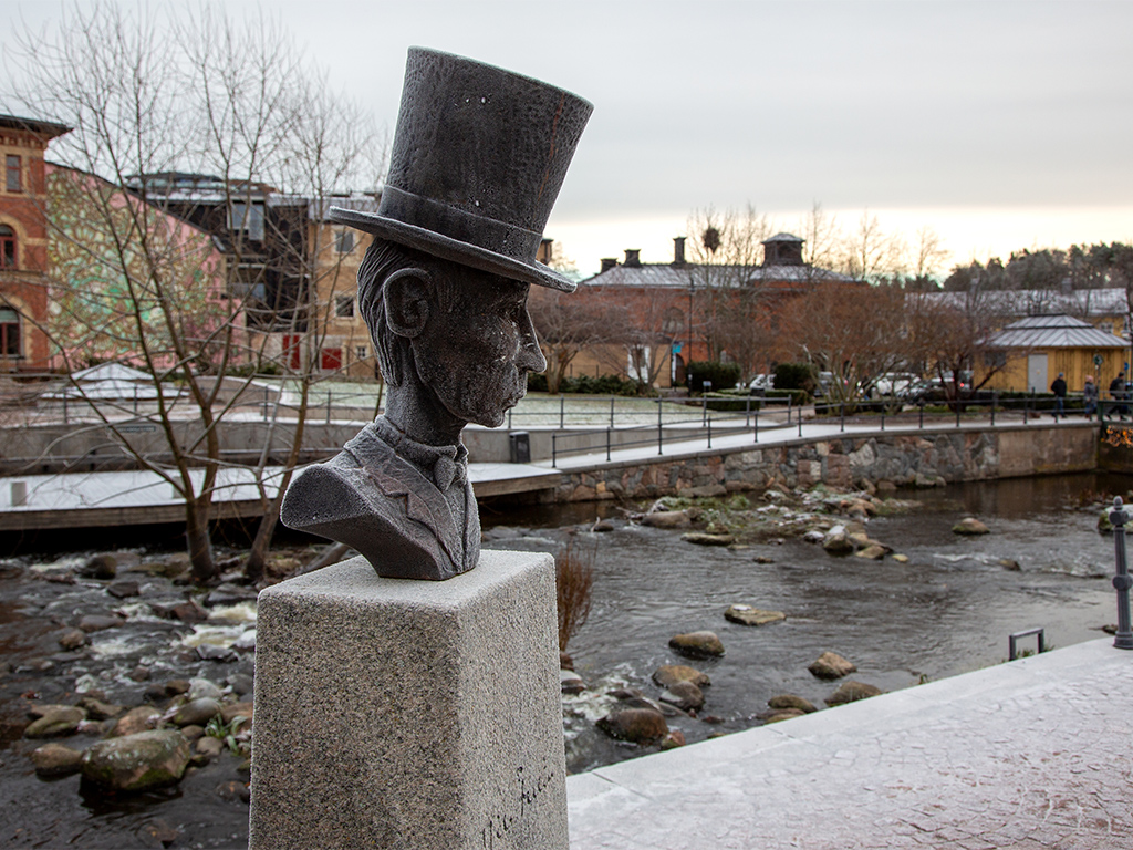 Skulptur och en byst av man i hög intill en å med forsande vatten.