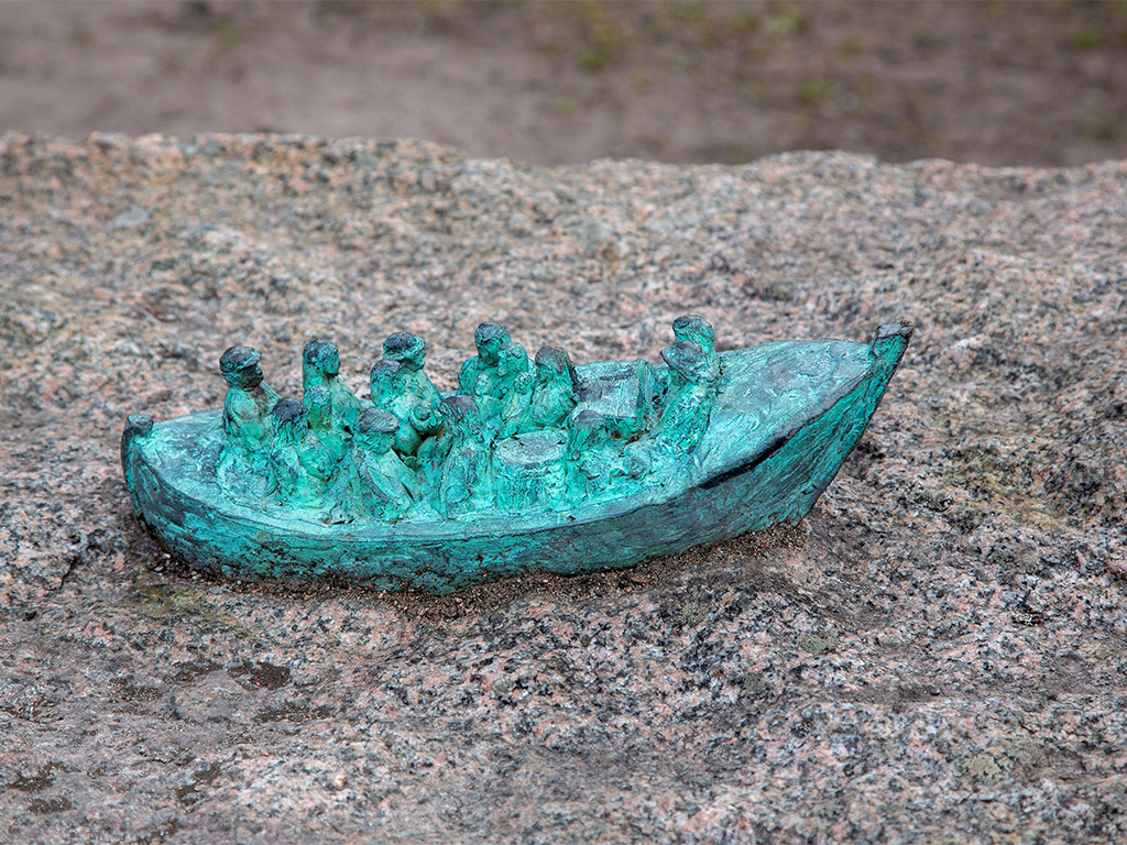 Skulptur av en liten grönaktig båt med människor på en stor sten.