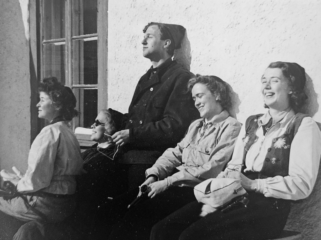 Fem personer sitter lutade mot en vägg med slutna ögon och näsorna mot solen.