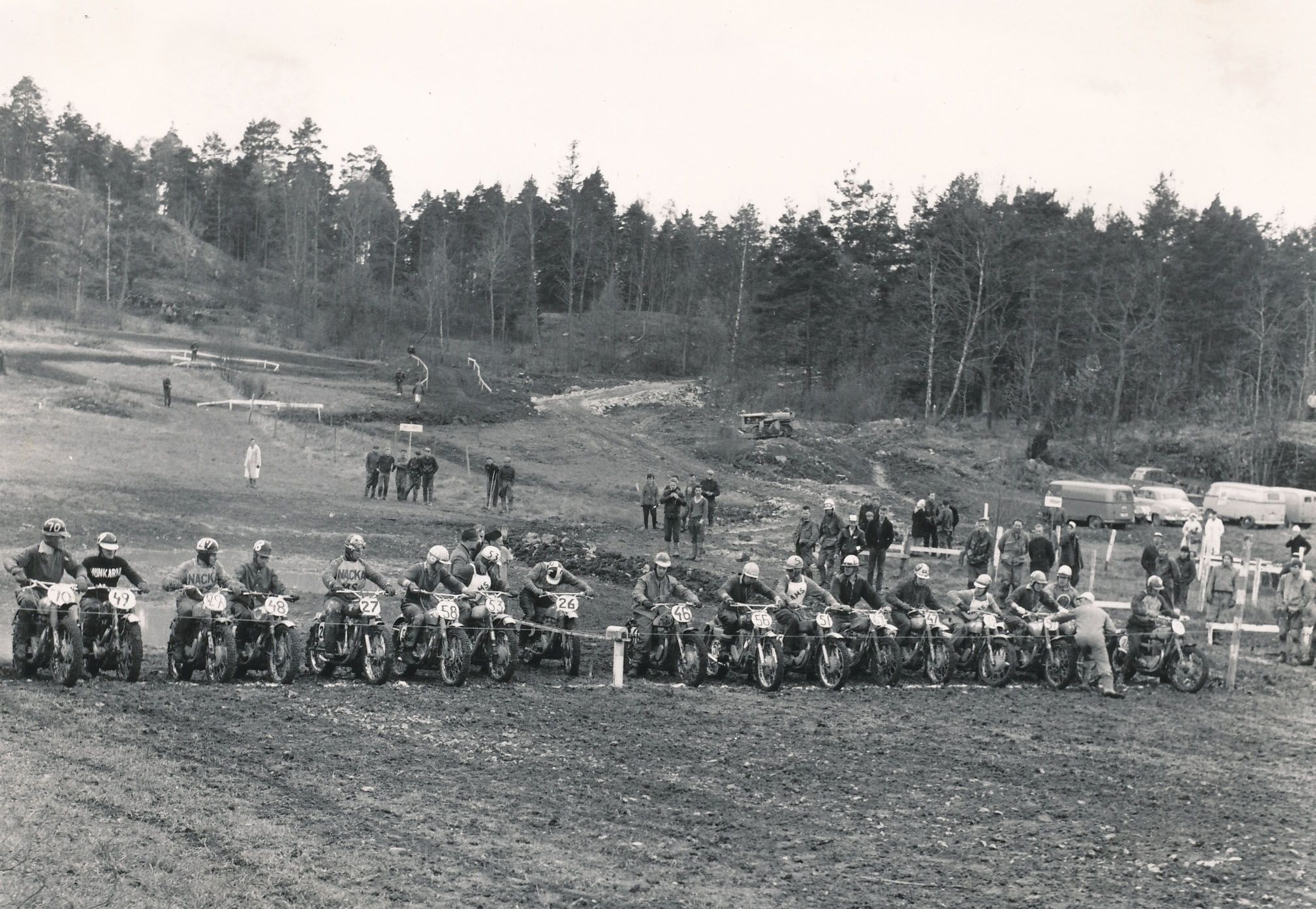 Många motorcrossförare står jämns med varandra på en lerig åker, snart går startskotten på tävlingen.