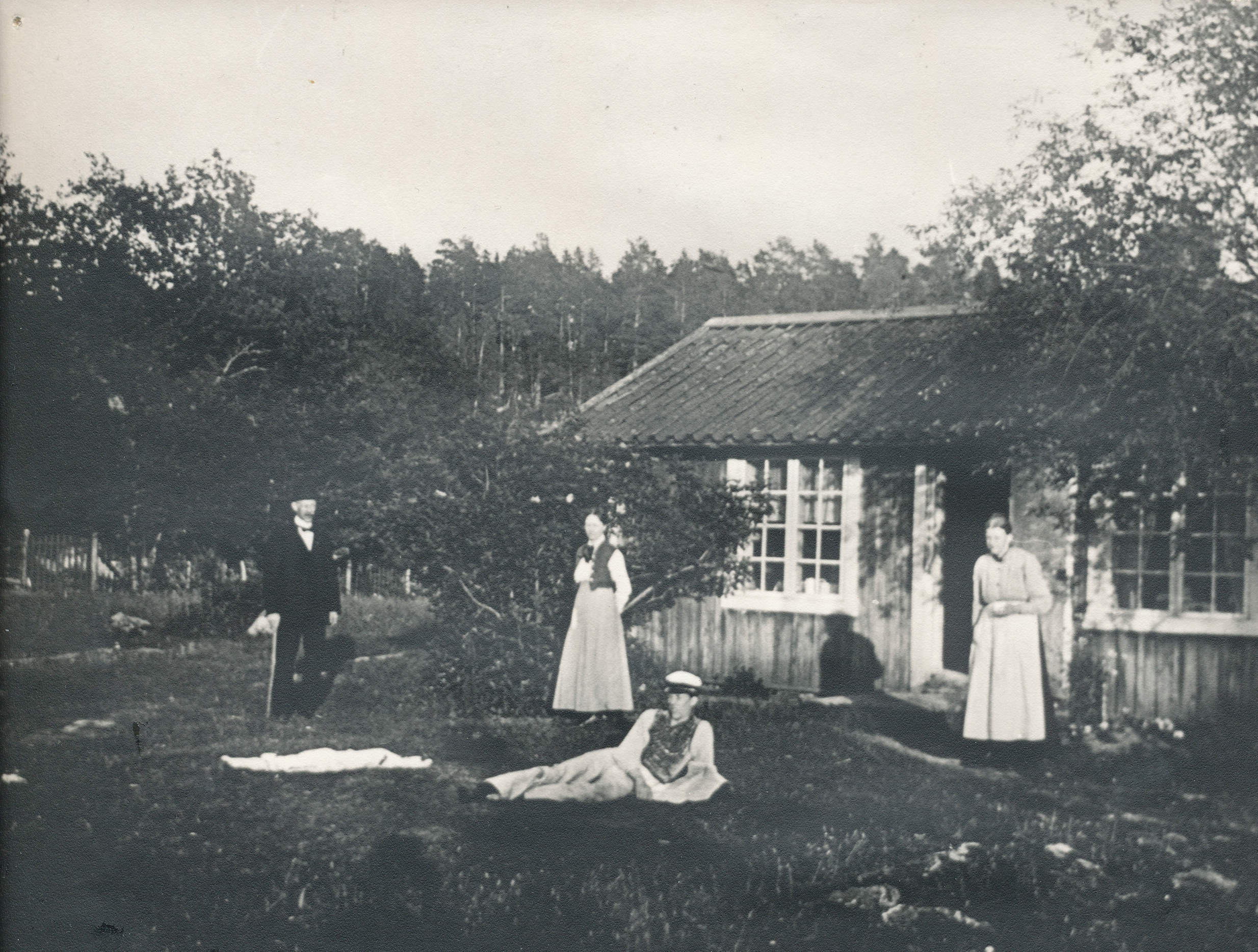 Fyra personer står framför ett litet hus, det är träd och grönska där de står.