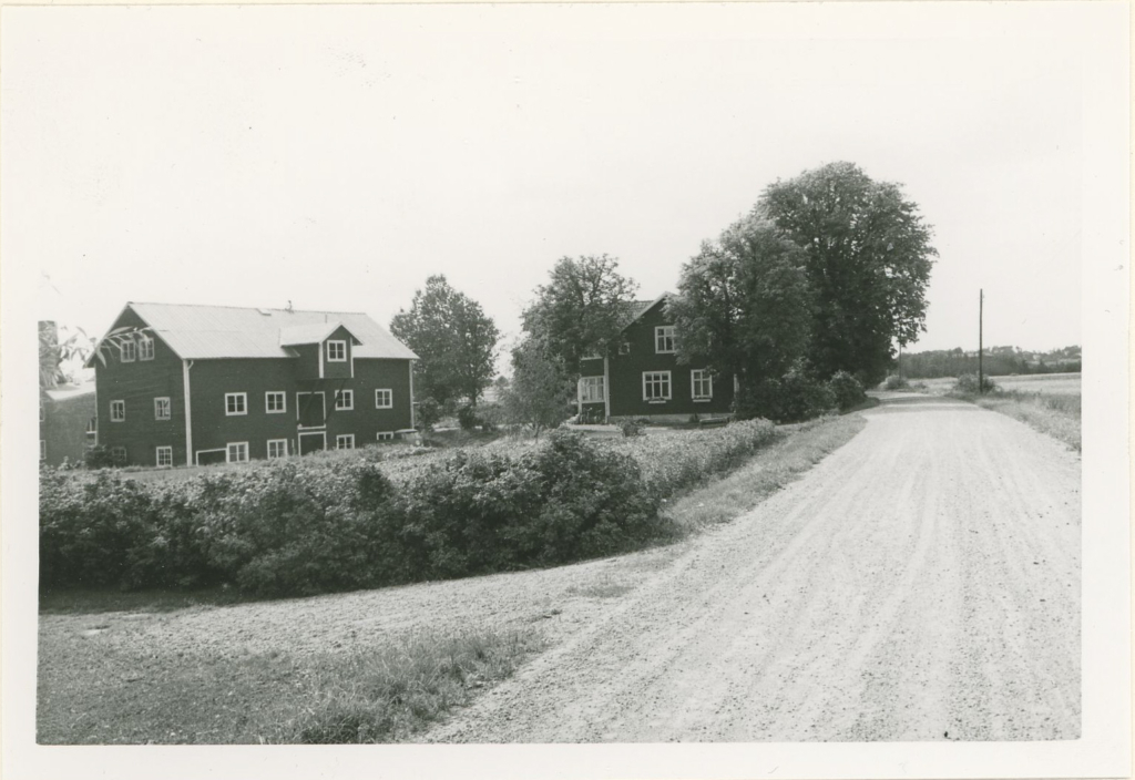 Två stora byggnader invid en grusväg.