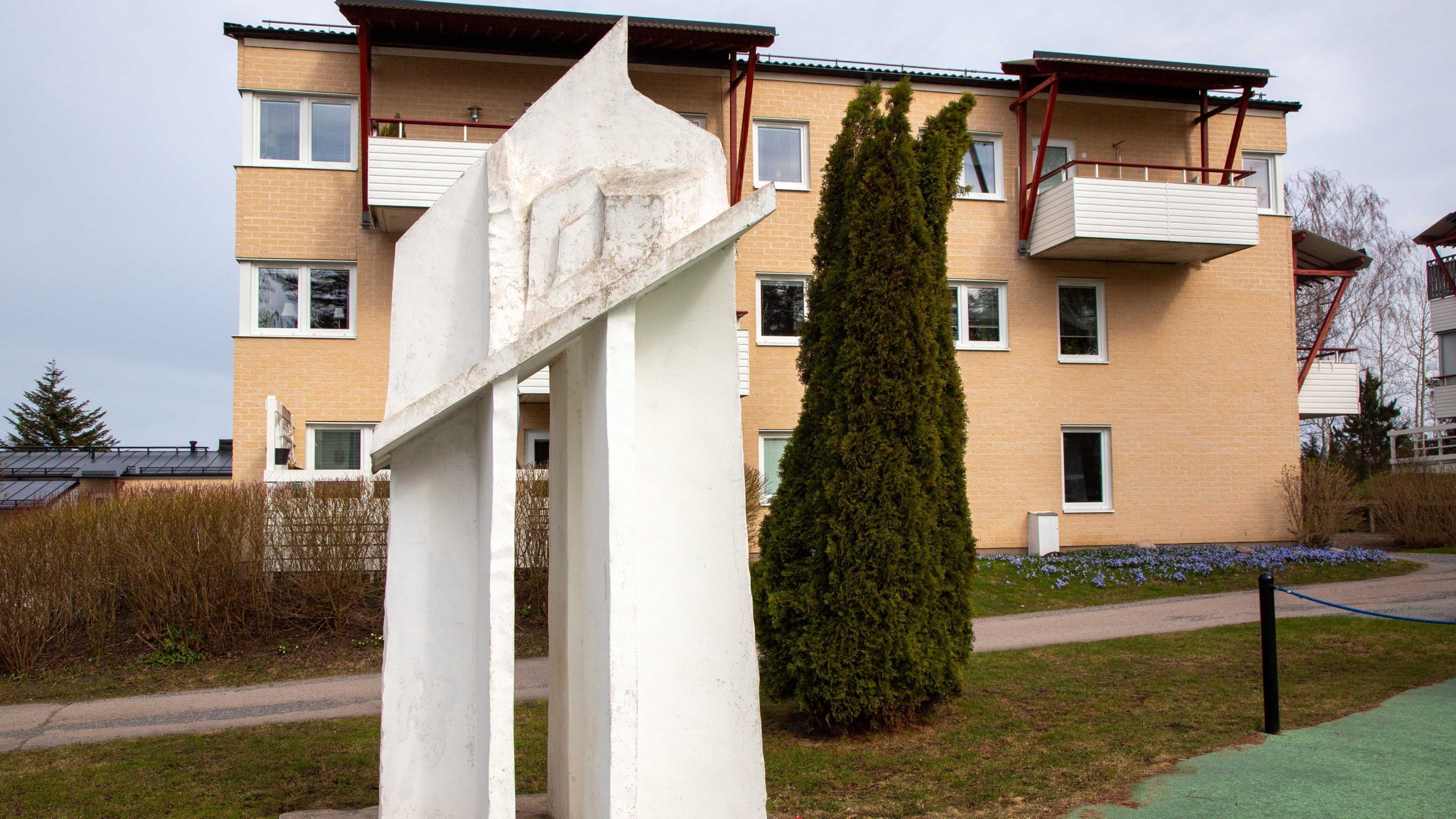 Hög vit skulptur med ett hålrum framför ett gult trevåningshus. bostadsområde